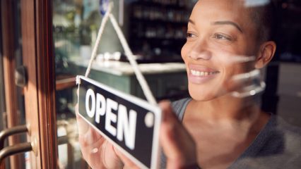 Women looking through a glass door of her business with an open sign in the window