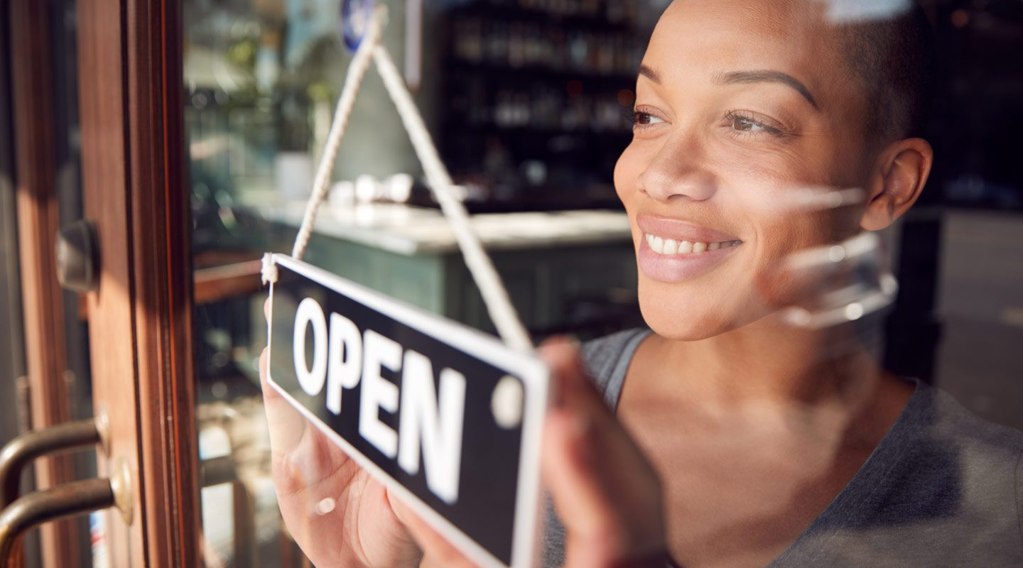 Women looking through a glass door of her business with an open sign in the window