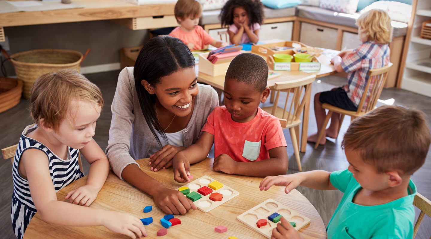 Children in a classroom sitting around a table with a teacher